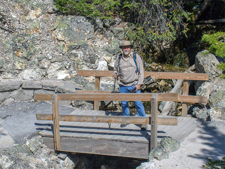 Les in hiking gear on a bridge with a walking stick